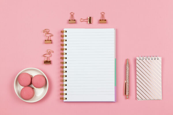 Modern female working space, top view. Notebooks, pen, clamps on pink backround, copy space, flat lay. Desktop of freelancer, student. Work from home, back to school, education concept. Horizontal